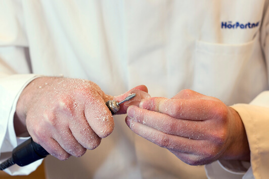 Ein Hörakustiker passt ein Ohrpassstück mit einem Fräswerkzeug individuell an.